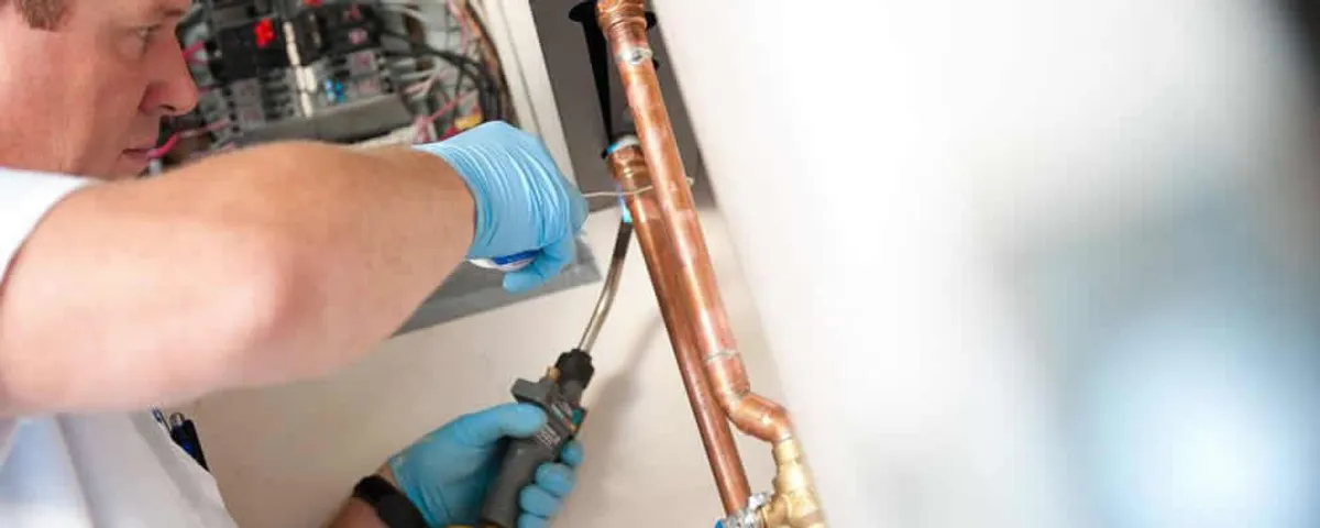 Water heater repair technician testing copper pipe connections and controls in San Diego, CA